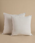 Cream square pillows against a beige background.