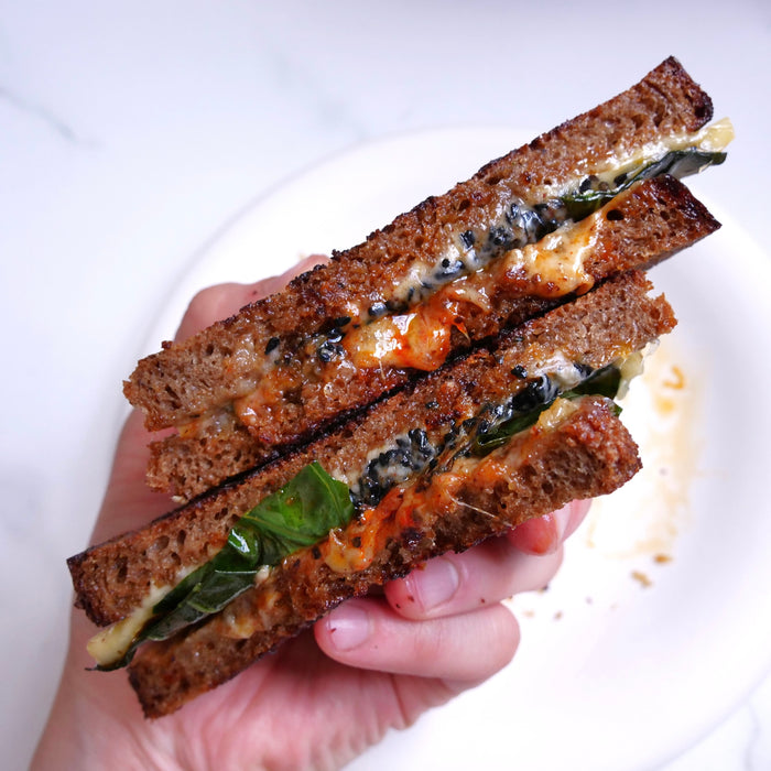 Hand holding a sandwich cut in half, with visible ingredients on a white plate.