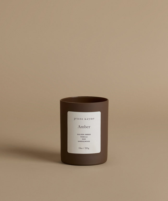 A glass candle with the scent Amber against a beige background.