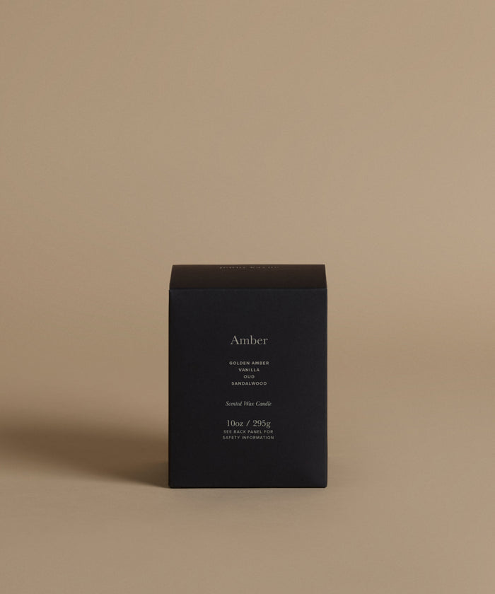 A candle box with the scent Amber across the front against a beige background.