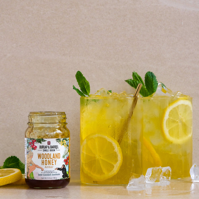 Two glasses of lemonade with mint leaves and a jar of Burlap & Barrel 'Woodland Honey' on a beige background