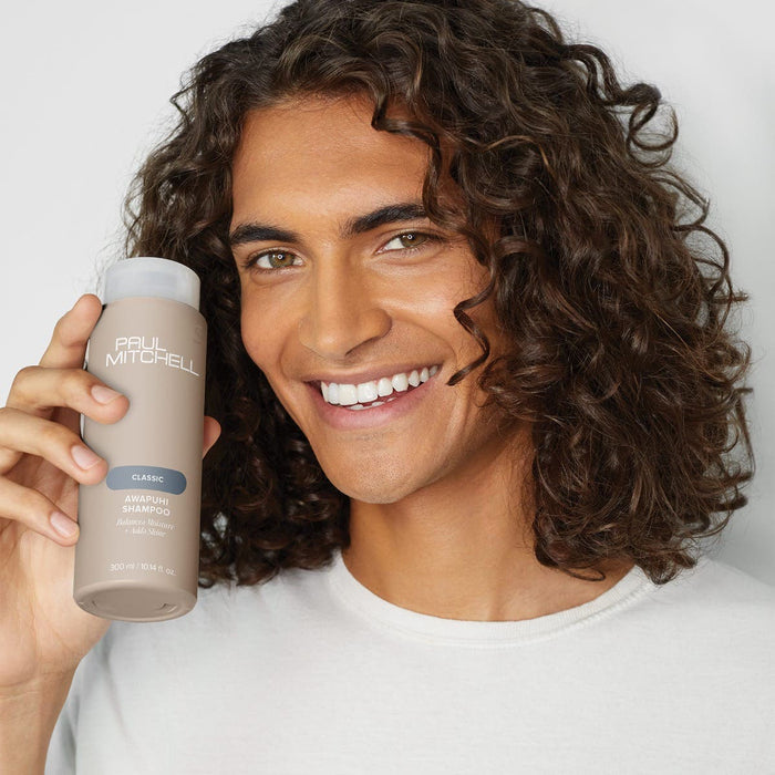 Male model with curly long hair holding bottle of Paul Mitchell Awapuhi Shampoo