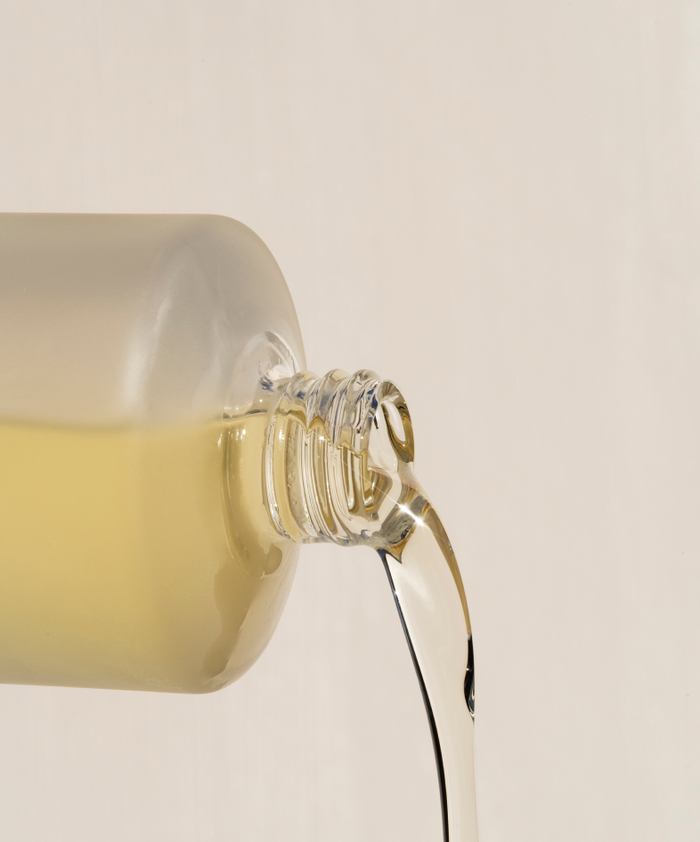 A close-up of a glass bottle pouring light yellow liquid against a plain background—perfect for highlighting the radiance and hydration benefits of Body Hydration Heroes.
