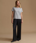A woman modeling a light gray short-sleeve crewneck t-shirt and black wide-leg trousers against a solid beige studio background.