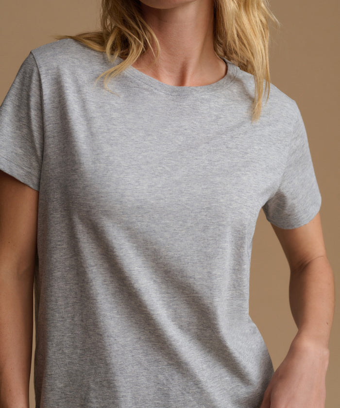 A close-up of a woman wearing a light heather gray short-sleeve crewneck t-shirt against a solid warm beige background.