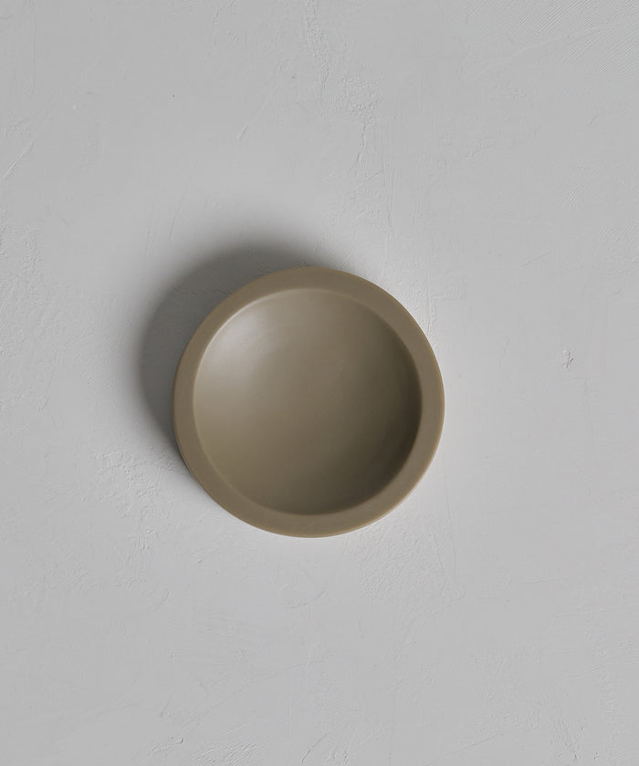 The Coast Soap Dish is a plain, round, light brown dish handcasted from resin and shown from above on a textured white background. Made in Mexico.