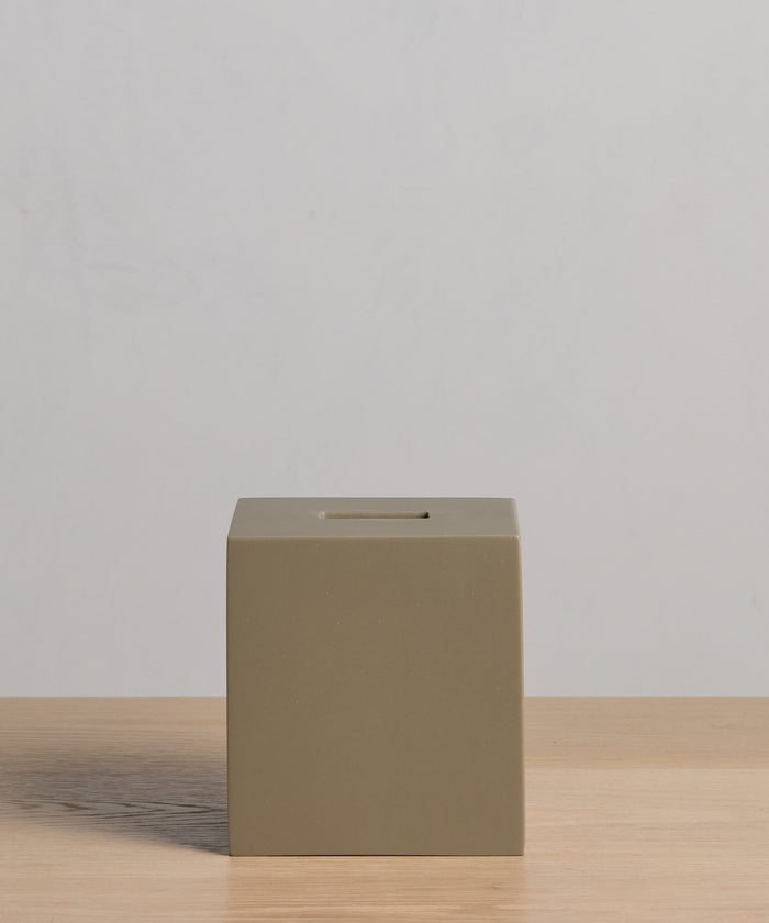 The Coast Tissue Cover, a simple, matte olive-green cube crafted from handcasted resin, sits on a light wooden surface against a plain light gray background.