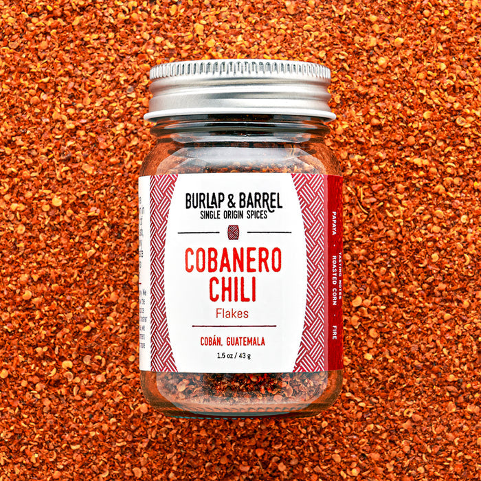 A jar of Cobanero Chili Flakes by Burlap & Barrel, placed on a background of expanded red chili flakes.