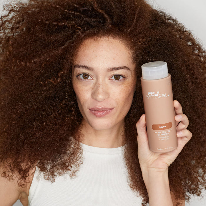 Image of model holding a bottle of Color Protect Shampoo near their face
