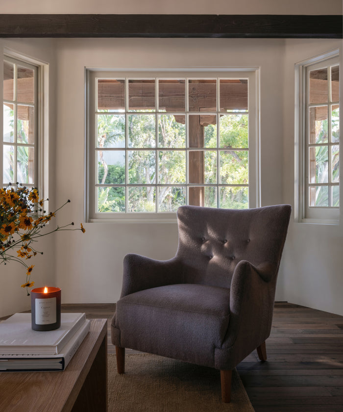 A living room setting with an accent chair, coffee table and a glass candle burning.