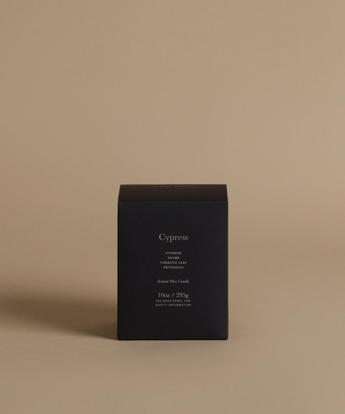 A candle box with the scent Cypress on the front against a beige background.