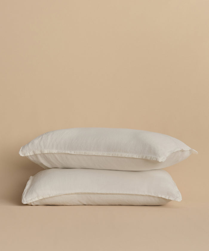 Two white pillows with Dusk Linen Pillow Sham Set of 2, stacked against a plain beige background.