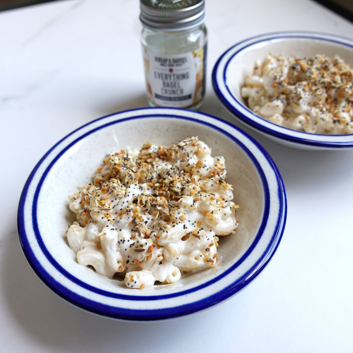 Two bowls of macaroni and cheese with a jar of seasoning on a white surface