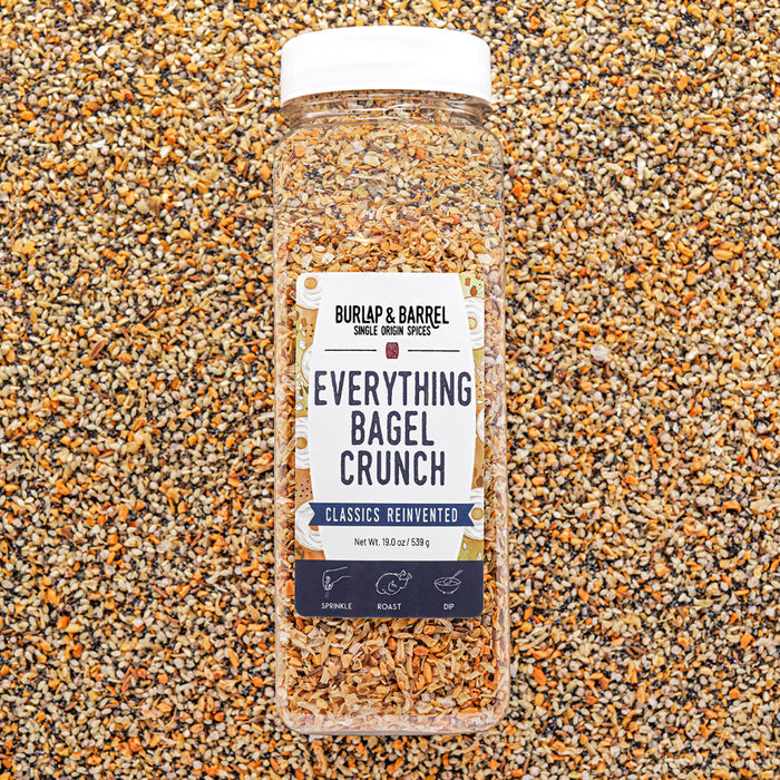 Container of Everything Bagel Crunch Seasoning from Burlap & Barrel on a bed of seeds and spices.