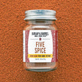 A glass jar with a metal lid labeled 'FIVE SPICE' from Burlap & Barrel on an orange textured background.