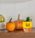 green seasonal snuffer, green hand-blown glass snuffer in pumpkin top and stem shape on a jack-o-lantern glassybaby on a kitchen shelf with gords.