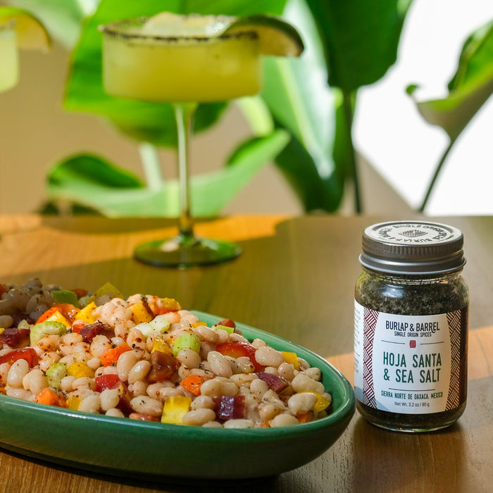 Jar of Hoja Santa & Sea Salt next to a bowl of bean salad on a table with a blurred background