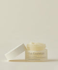 A small glass jar of Hydra Eye Balm with a white lid beside it sits open, displaying its creamy, hydrating formula that helps reduce puffiness, all set against a neutral background.
