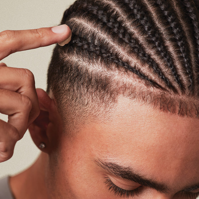 Close-up of a person's hand pointing to a freshly styled hairline with braided hair with a little product on their finger.