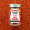 Jar of Burlap & Barrel Low & Slow Chili Powder on a textured brown background