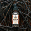 A bottle of Burlap & Barrel Vanilla Extract with Rum & Bourbon, featuring a dark dropper cap and cream label, set against a background of dried vanilla beans.