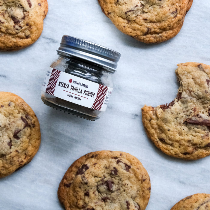 Jar of vanilla powder surrounded by chocolate chip cookies on a marble surface