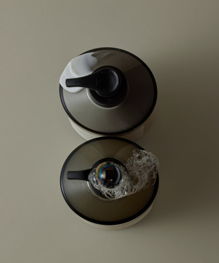 Two soap dispensers with black nozzles on a beige background