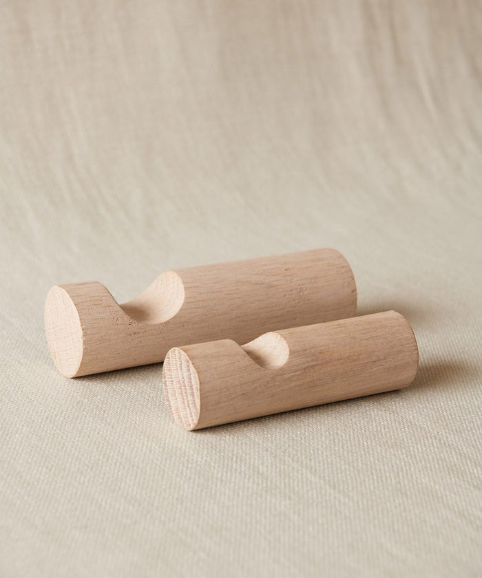 Two Oak Wall Hooks with a smooth finish and scooped notches rest on textured light beige fabric, highlighting the rustic craftsmanship of the white oak.