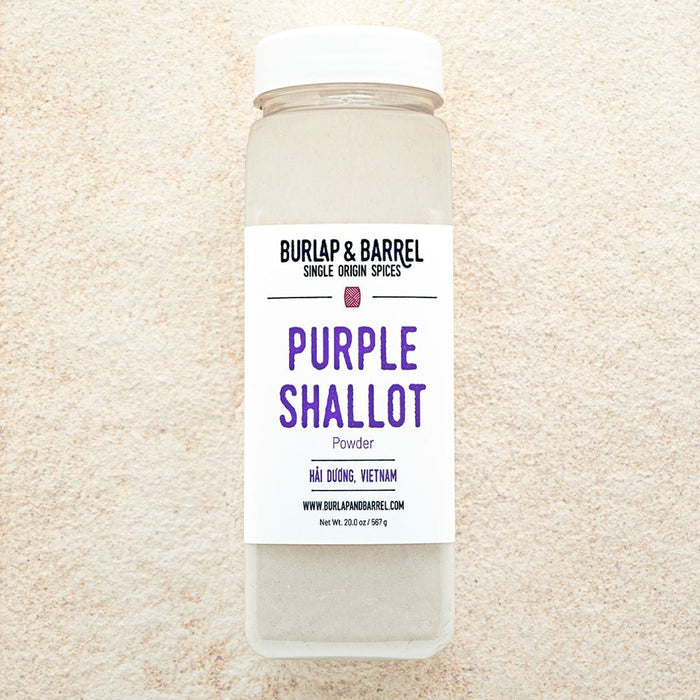 A container of Purple Shallot Powder by Burlap & Barrel, displayed on a background of beige powder.