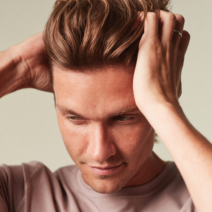 Man adjusting his hair against a neutral background