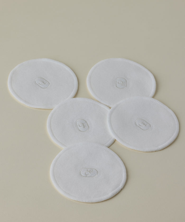 Five Reusable Cotton Rounds are arranged on a light beige surface, slightly overlapping. Each white, round pad features central oval stitching, making them perfect for elevating your cleansing routine.