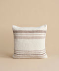 The Sheridan Pillow, a square cushion featuring horizontal beige and light brown stripes on white alpaca blend yarn, is shown upright against a plain beige background.