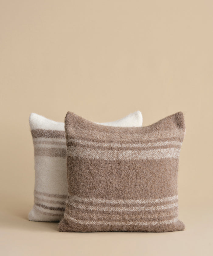Two textured throw pillows with horizontal stripes, one in taupe and cream and one in off-white and taupe, set against a solid beige background.