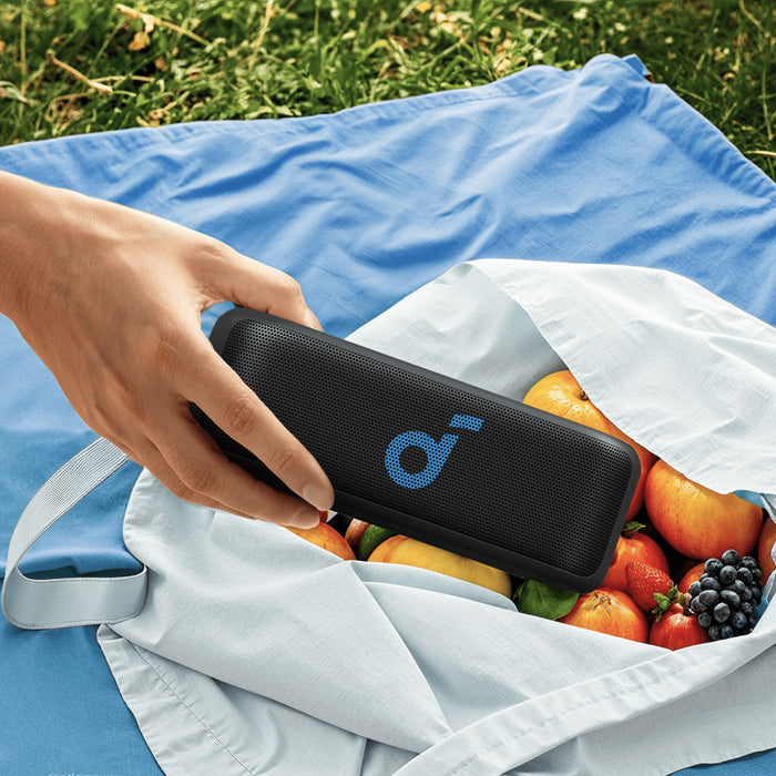 hand holding soundcore portable speaker with blue logo for picnic