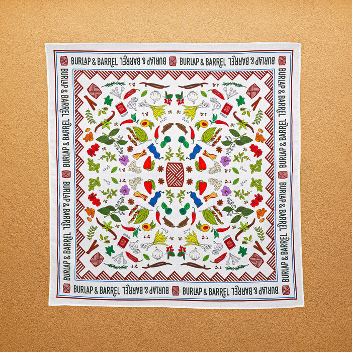 A multicolored, 100% cotton bandana with hand-drawn spice illustrations laid out flat on a surface.