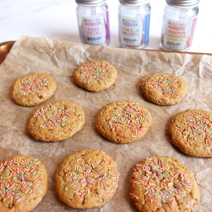Cookies with colorful Burlap & Barrel spiced sprinkles on top of them on a baking tray with parchment paper. Sprinkle jars are behind.