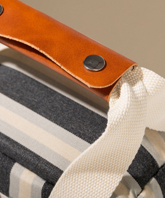 Close-up of a bag with a brown leather handle and striped fabric.
