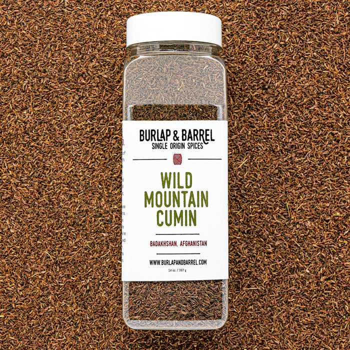 Plastic container of wild mountain cumin from Burlap & Barrel on a background of loose cumin seeds.